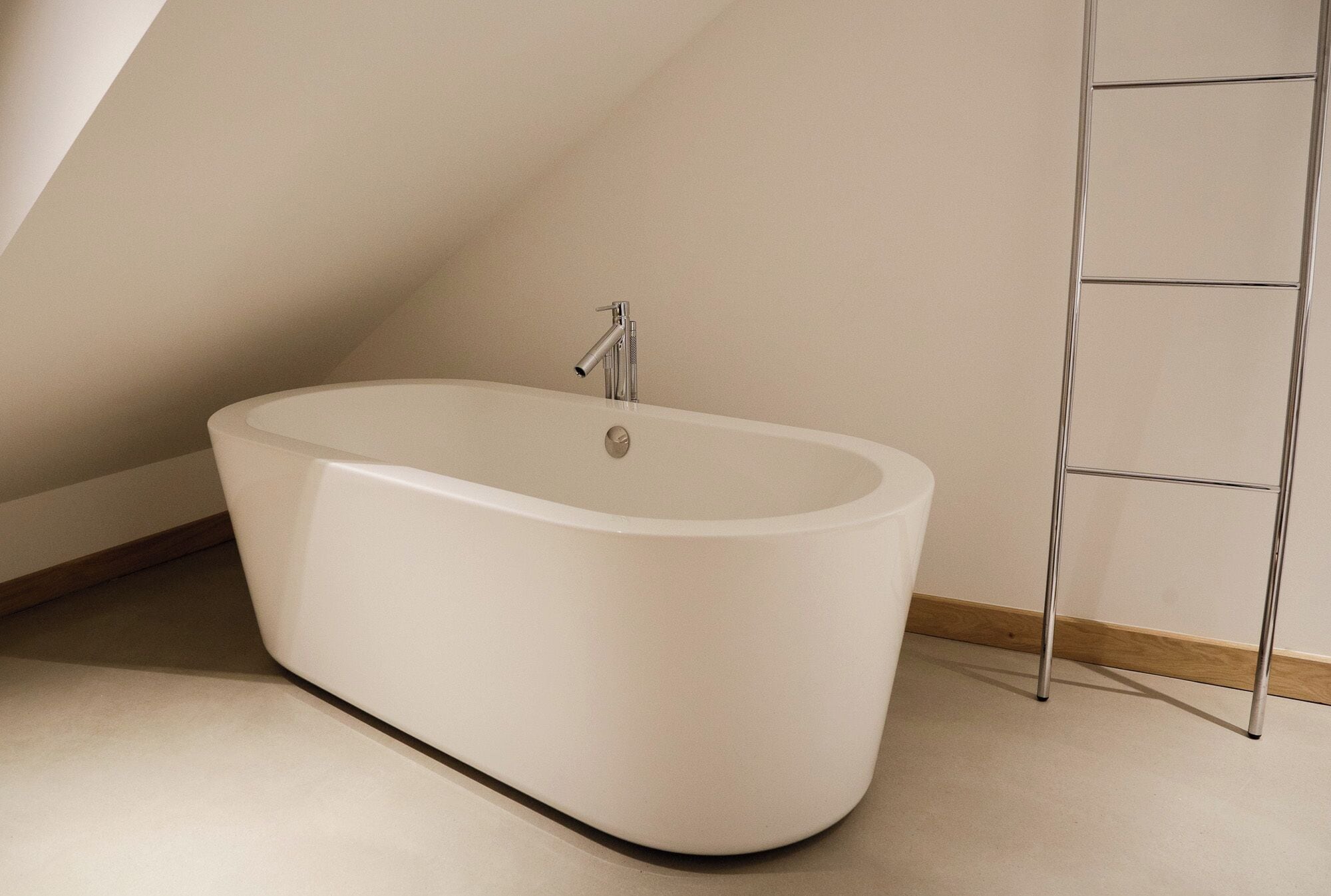 Une baignoire moderne, autoportante, placée dans un coin d’une pièce dotée d’un plafond en pente et d’un plancher en bois.