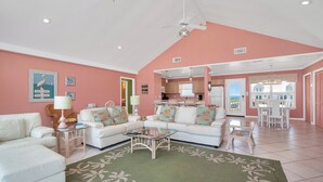 A spacious living room with a high ceiling, white sofas, a glass coffee table, and a green patterned rug. - Beautiful Gulf Front Home With Amazing Views! (Gulf Shores)