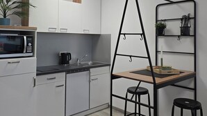 Una cucina moderna con mobili bianchi, un forno a microonde, una macchina da caffè e un piccolo angolo ristoro con sgabelli e uno scaffale.