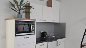 Una cucina moderna con mobili bianchi, un forno a microonde, una macchina da caffè e una pianta in vaso.