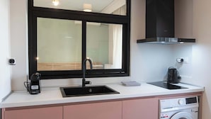 A compact kitchen with a sink, a coffee maker, a microwave, and a built-in washing machine.