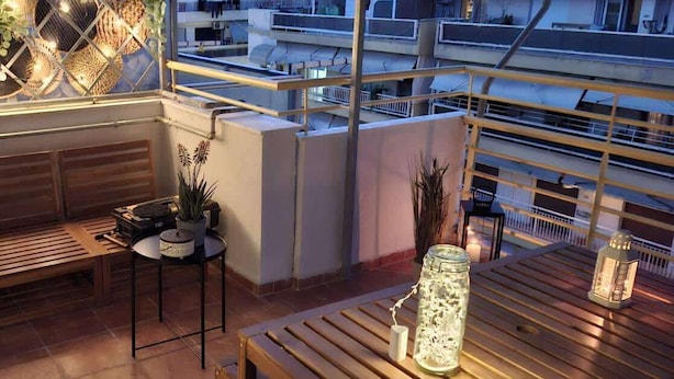 A rooftop terrace with a wooden table, chairs, a small table with a potted plant, and a decorative lantern.