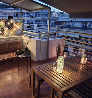 Eine Dachterrasse mit einem Holztisch, Stühlen, einem kleinen Tisch mit einem Topfpflanzen und einer Zierleuchte.