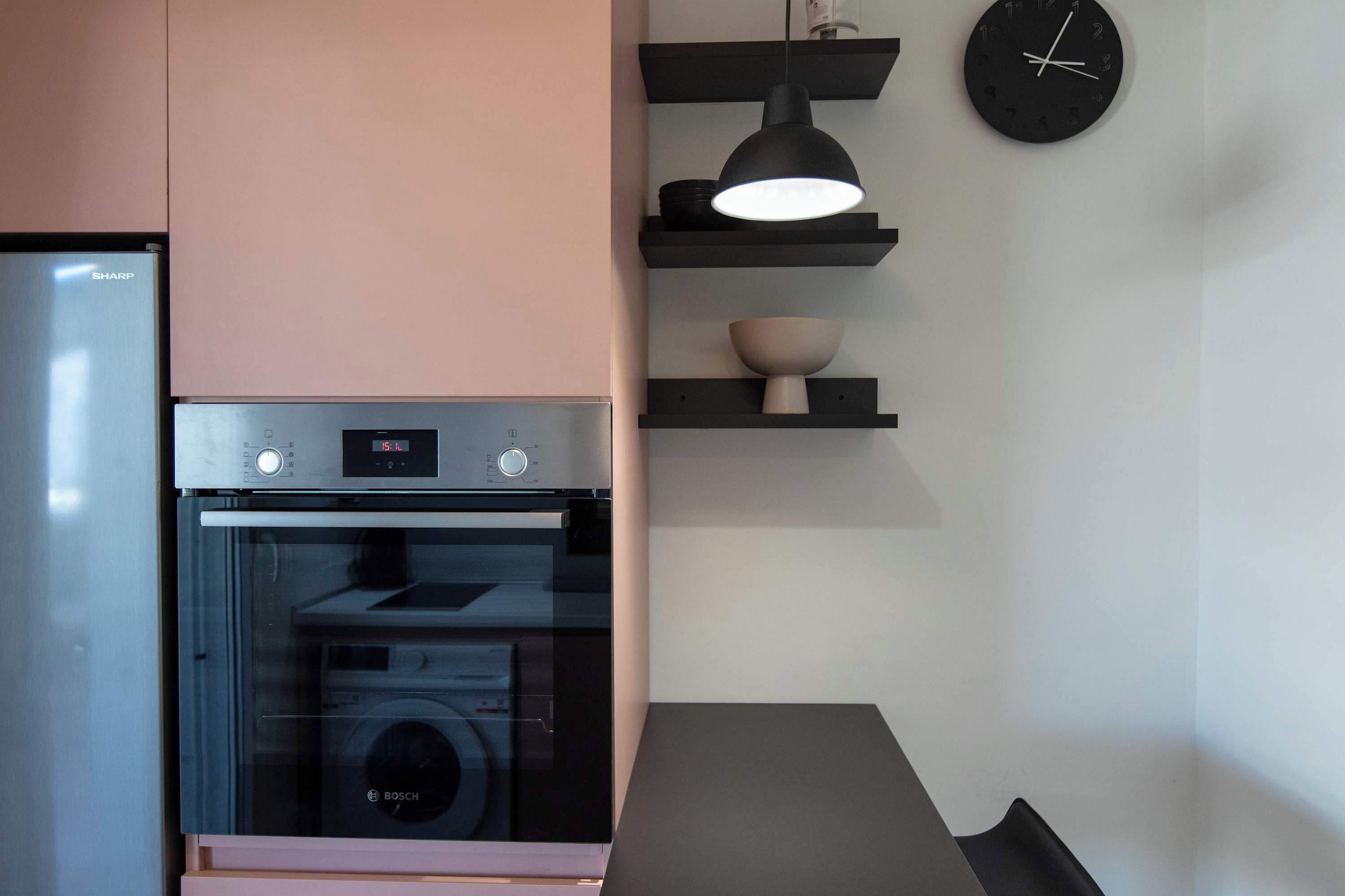 Una cocina con un horno Bosch, un refrigerador Sharp y un reloj negro en la pared.