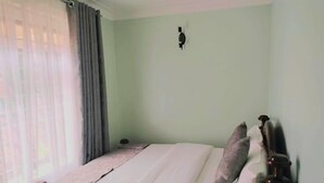 A bedroom with a bed, a nightstand, and a wall-mounted light fixture. - Crux hotel  (Kampala)