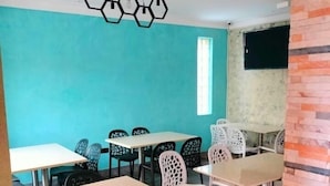A dining area with multiple tables and chairs, a teal wall, and a brick accent wall. - Crux hotel  (Kampala)