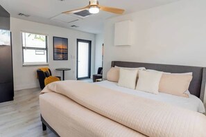 Habitación de hotel moderna con una cama grande, ventilador de techo, una mesita y una silla.