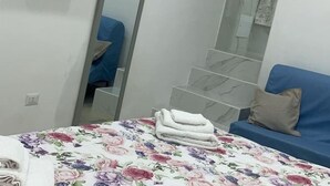 A hotel room with a bed covered in a floral bedspread, a blue sofa with a beige pillow, and a mirror reflecting part of the room. - Guazzo Home b&b Rione Sanità  (Napoli)