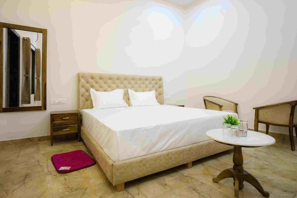 A bedroom with a large bed, a bedside table, a small round table, and a chair. - Gulmohar Retreat And Spa (Kumbhalgarh)