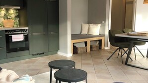 Un soggiorno moderno con un divano verde scuro, due tavolini neri, una panca in legno e un'area pranzo con tavolo e sedie.