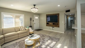 Ein Wohnzimmer mit beiger Couch, weißem Couchtisch, einer Kronleuchter, einem flachbildfernseher an der Wand und einer Holz-Unterhaltungsanlage.