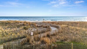 Ein Sandstrand mit Holzzaun und einem Hinweisschild für den Übergang durch die Düne.