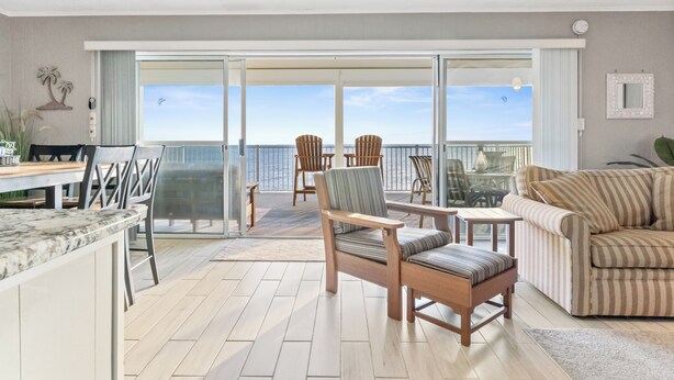 Ein geräumiger Balkon mit Meerblick, ausgestattet mit einer Couch, Stühlen und einem Esstisch.