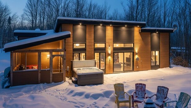 Una cabaña moderna con jacuzzi, fachada de madera y terreno cubierto de nieve.