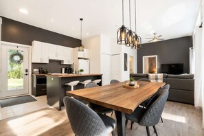 A modern kitchen with white cabinets, a wooden dining table, and a built-in island.