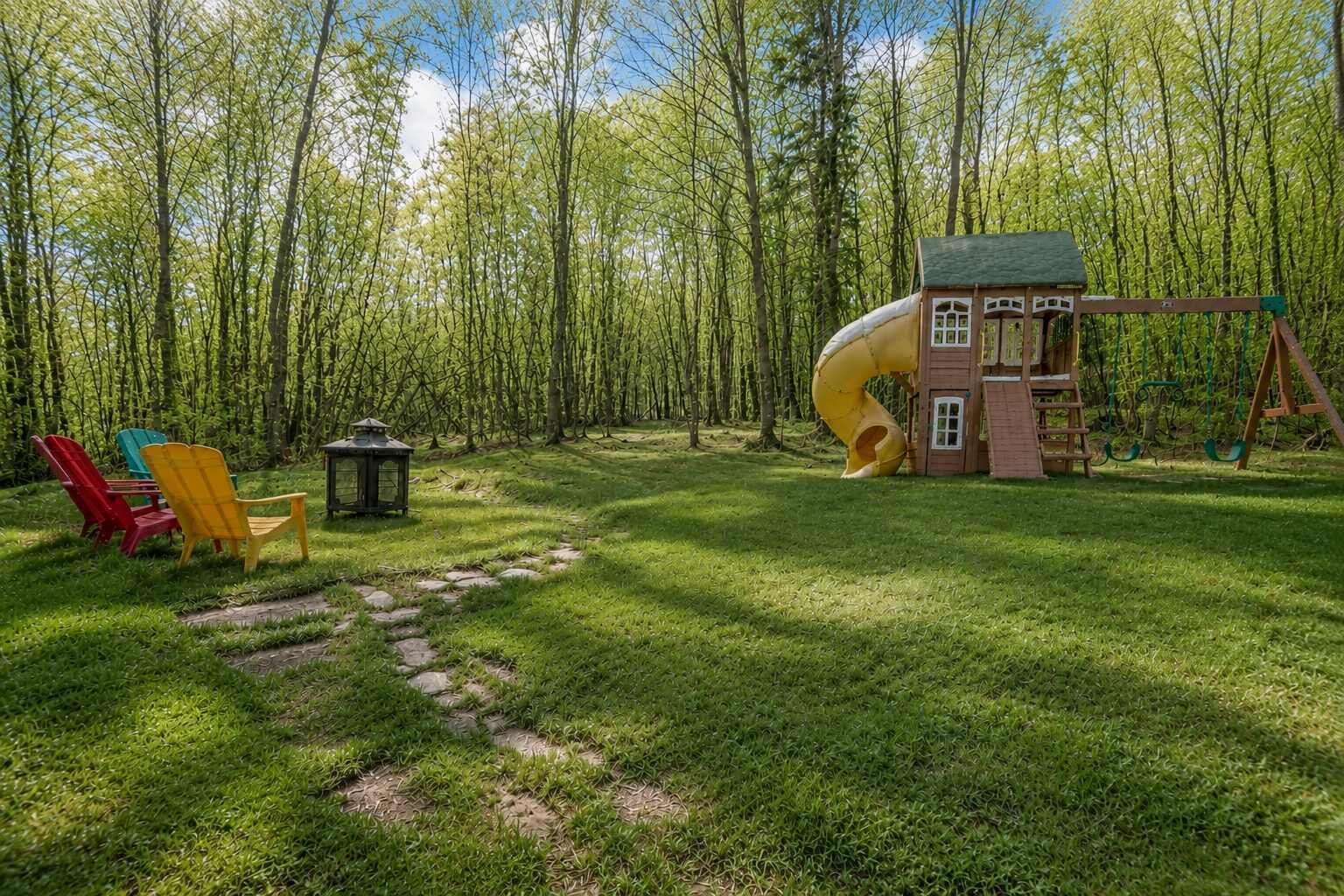 A playground with a slide and swings, surrounded by a grassy area with Adirondack chairs and a lantern.