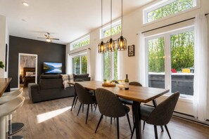 A modern dining area with a wooden table, dark chairs, and pendant lighting.