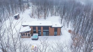 Un edificio moderno de dos pisos con techo nevado, rodeado por un bosque.