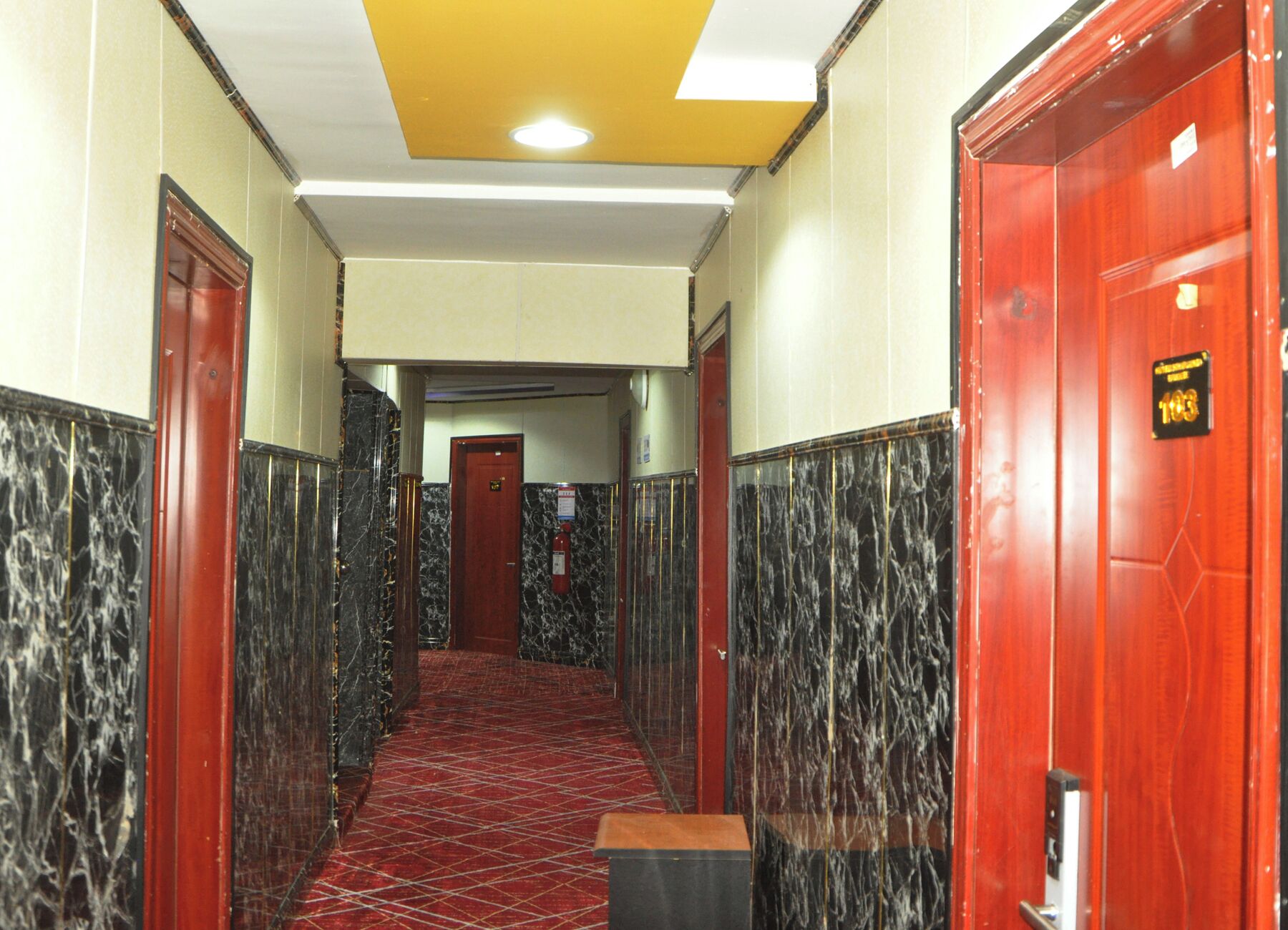 A hallway with marble walls, a red carpet, and a yellow ceiling.