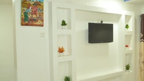 A living room with a mounted TV, white walls, and built-in shelving with plants.