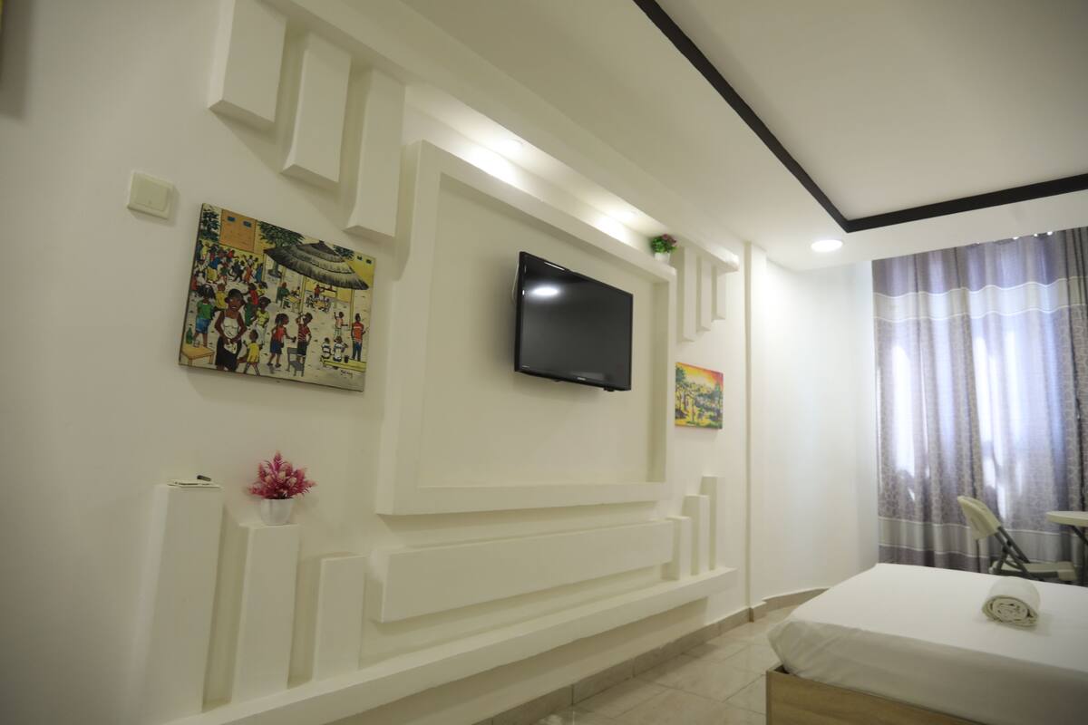 Une chambre d’hôtel équipée d’un téléviseur à écran plat fixé au mur, d’un lit recouvert d’une courtepointe blanche, d’une petite table et d’une chaise.