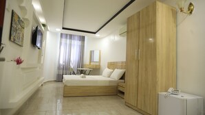 A bedroom with a bed, wardrobe, desk, chair, and a small white appliance.