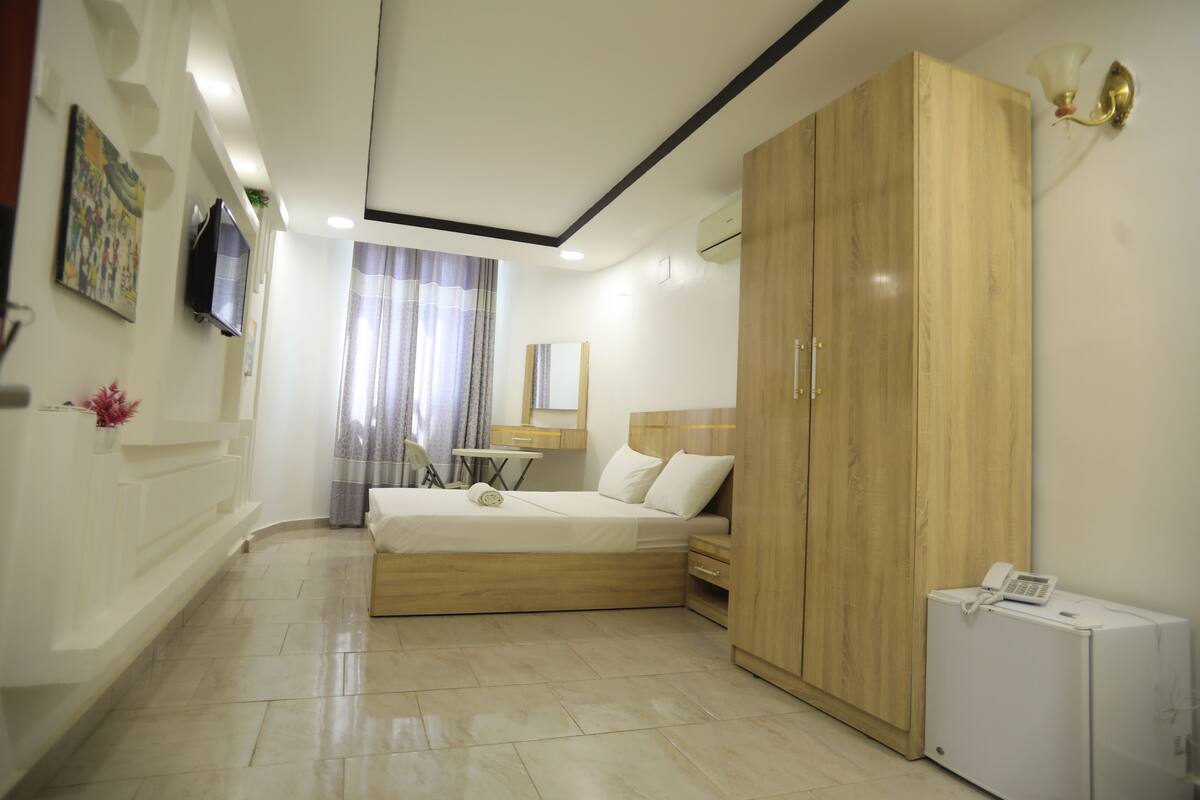 Une chambre à coucher comprenant un lit, une armoire, un bureau, une chaise et un petit appareil électroménager blanc.