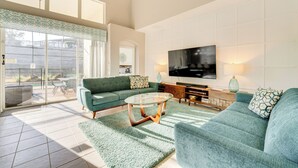 A spacious living room with a green sofa, a glass coffee table, and a flat-screen TV on a white wall. - 3 Mi to Disney: Family-friendly Home! (Kissimmee)