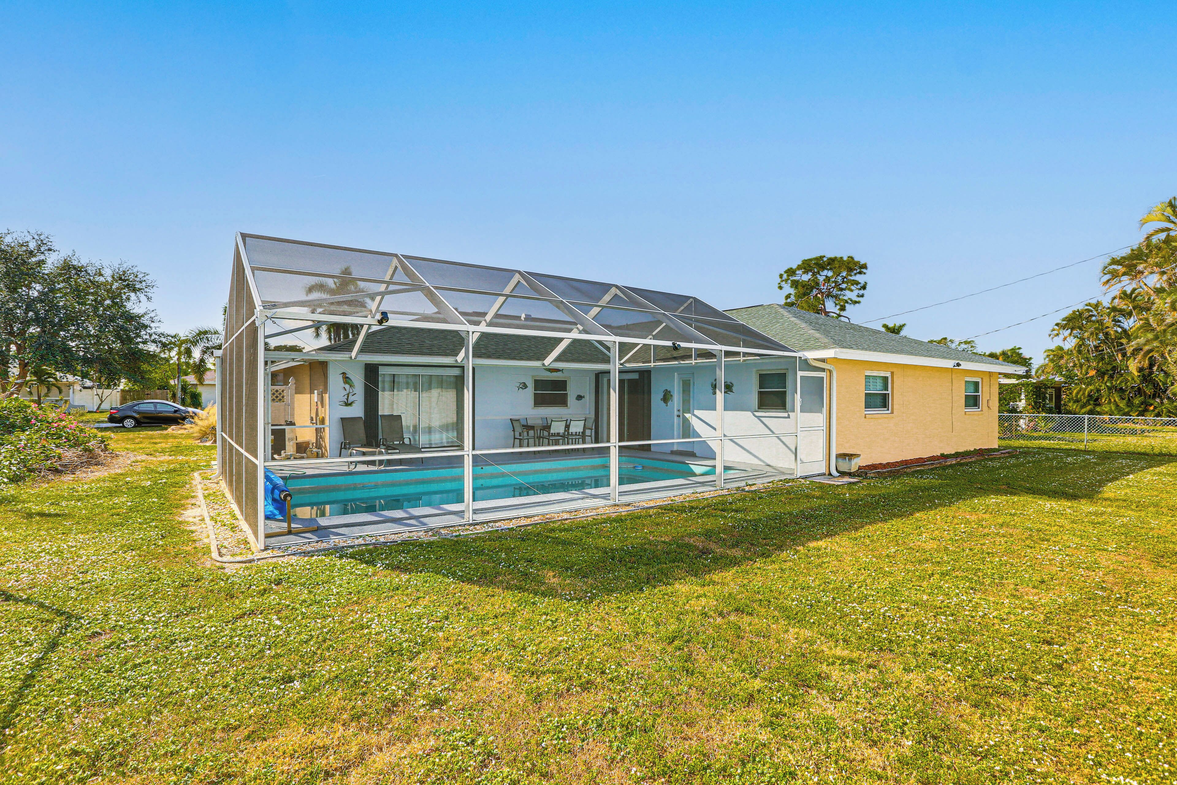 A house with a glass-enclosed swimming pool, a patio, and a car parked nearby.