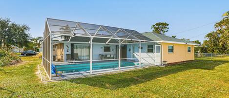 A house with a glass-enclosed swimming pool, a patio, and a car parked nearby.