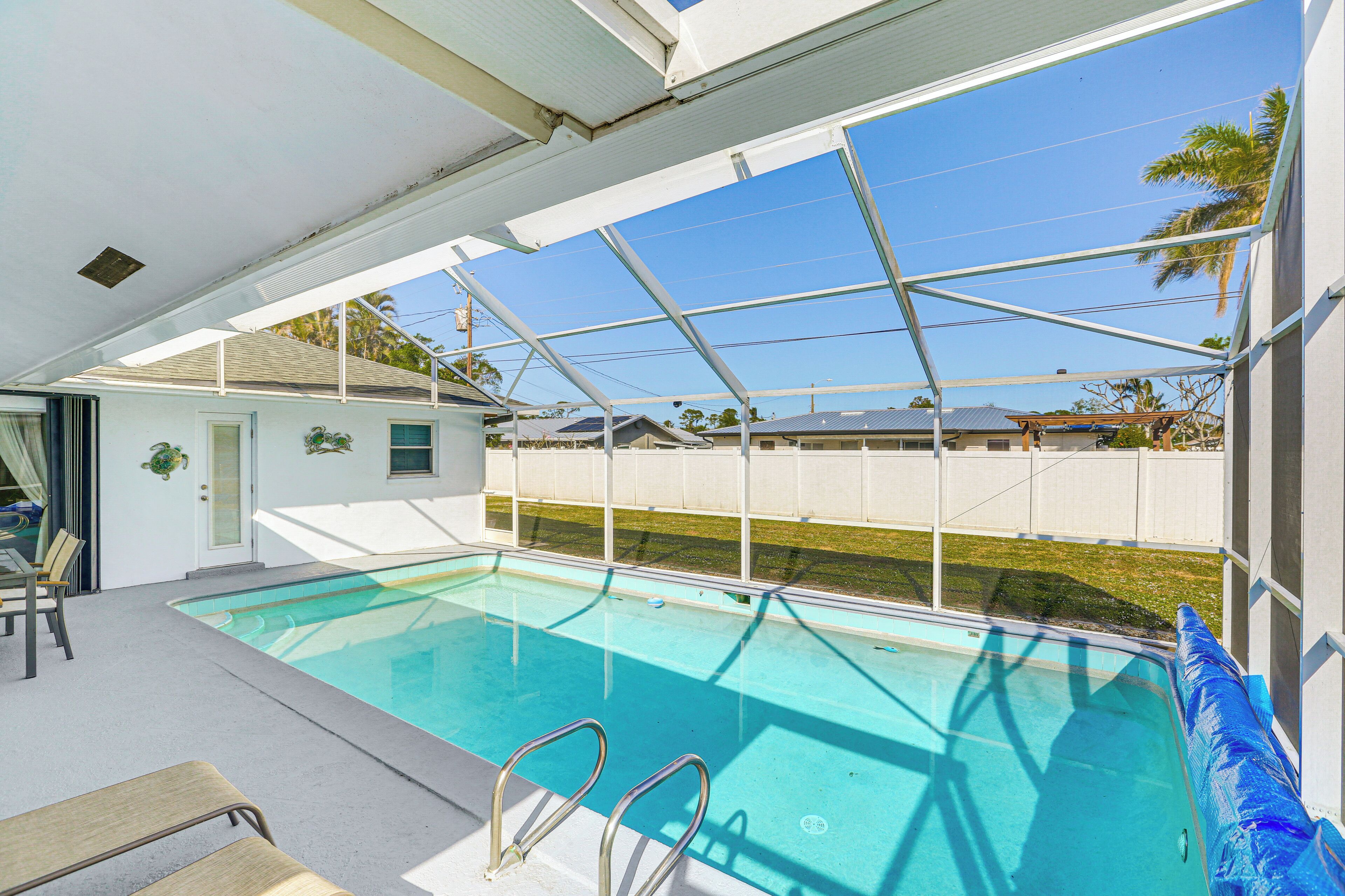 A swimming pool with a covered area, clear blue water, and a view of neighboring houses.