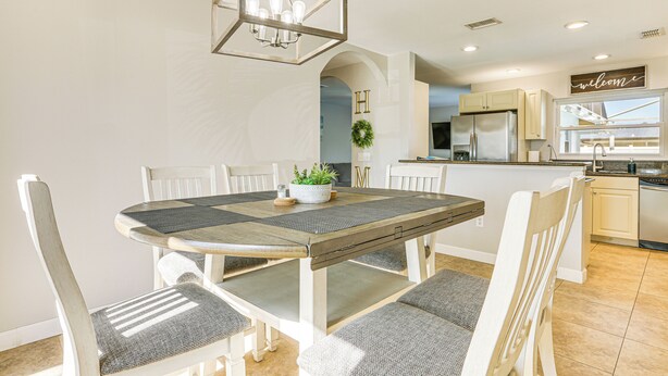 A dining area with a wooden table and chairs, a chandelier, and a kitchen in the background. - 4 Mi to Lakes Park: Family Home in Fort Myers! (Fort Myers)