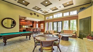 A spacious room with a pool table, a billiards table, a round dining table with chairs, a sofa, and a large window with a view of greenery.