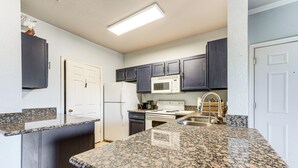 A kitchen with dark cabinets, a white refrigerator, a microwave, and a granite countertop.