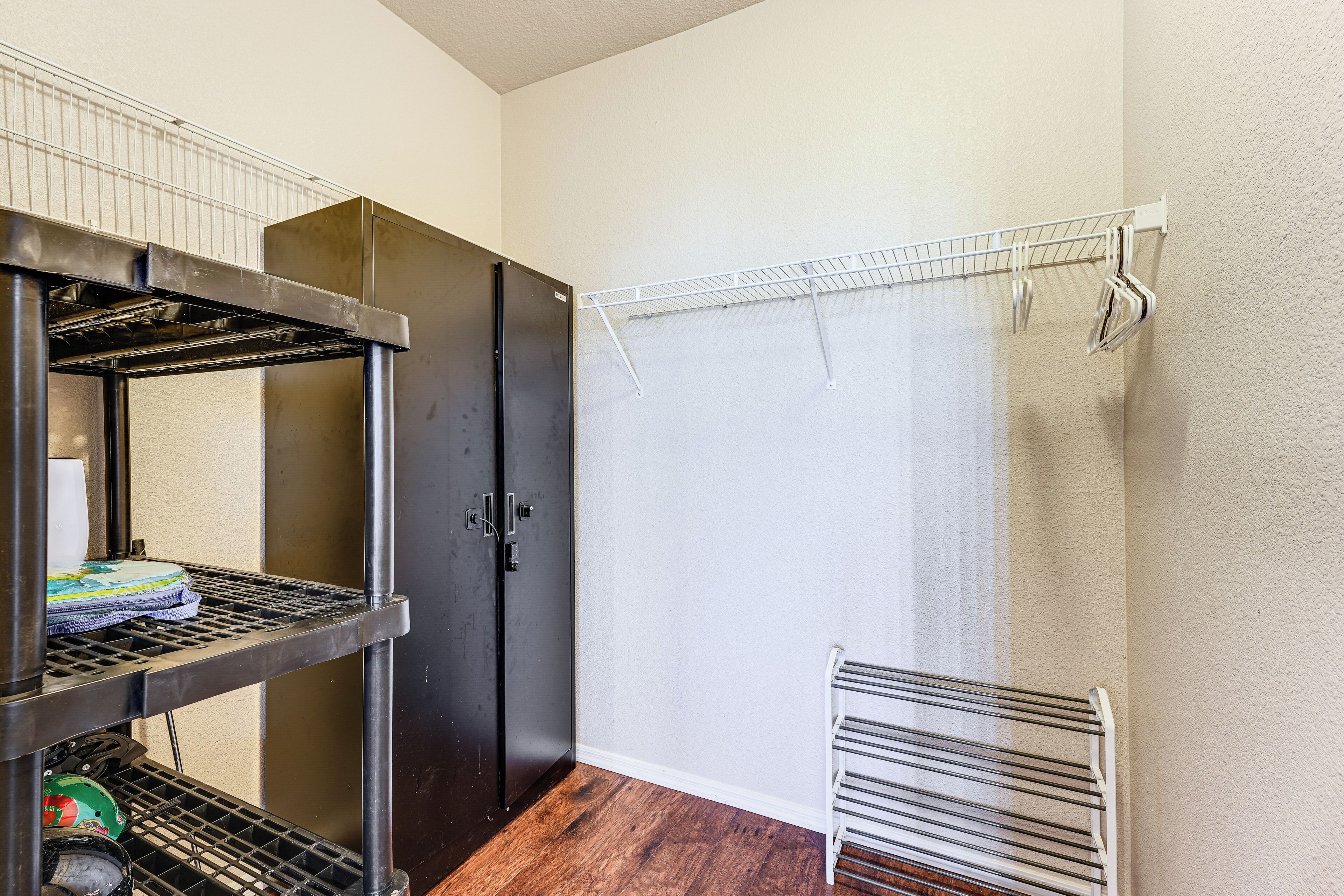 A compact room with a black refrigerator, a metal rack with items, a white radiator, and a window with a white curtain.
