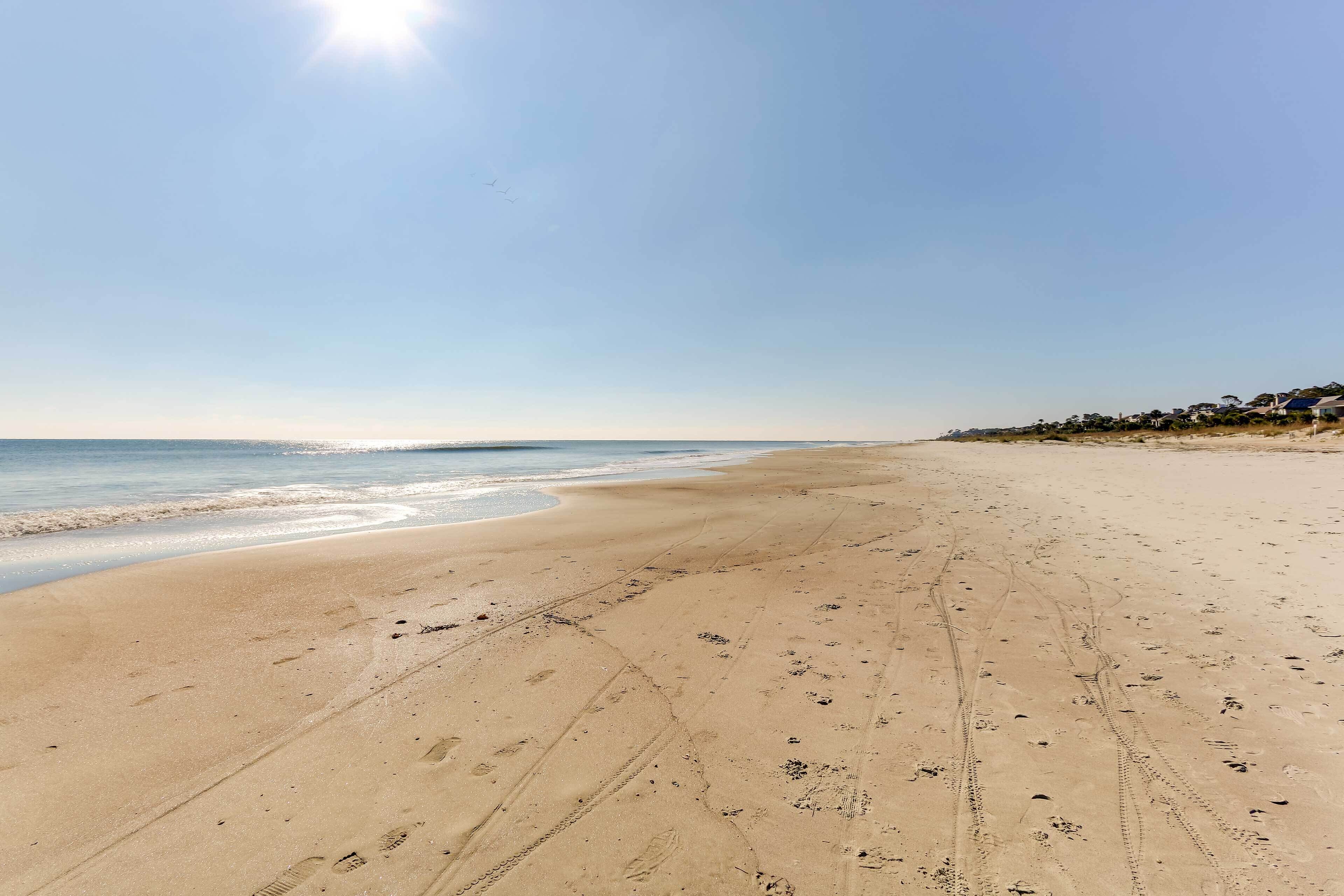 A wide sandy beach with footprints and tire tracks, leading to the ocean.