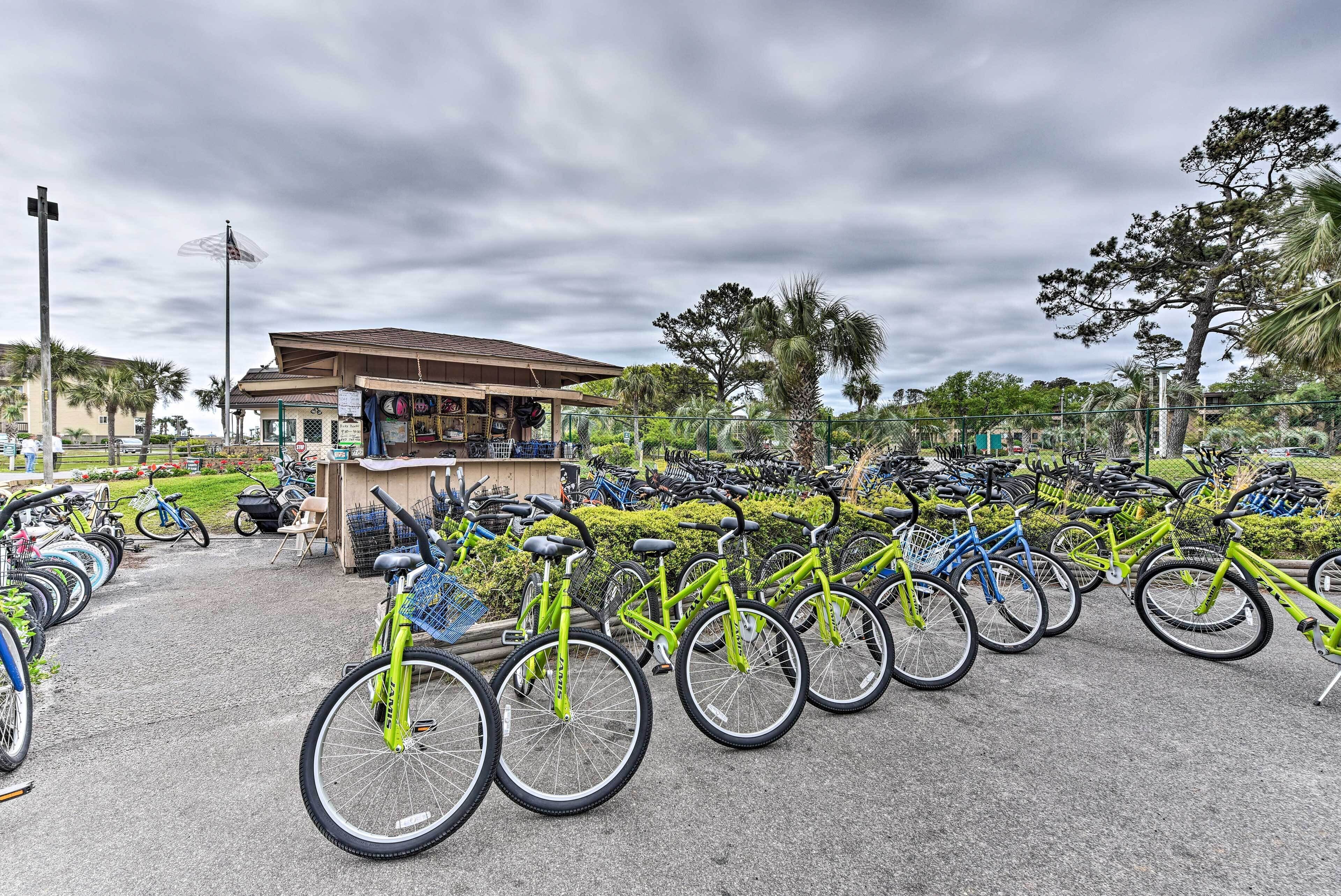 A bicycle parking area with multiple bicycles, a small kiosk, and a building with a sloped roof.