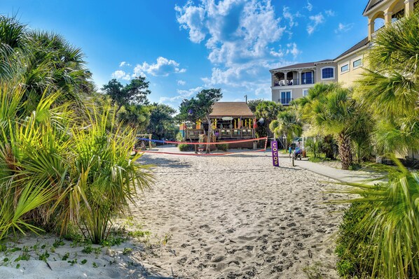 Une plage avec un filet de volley-ball, des palmiers et un bâtiment doté de balcons.