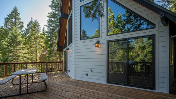 A wooden deck with picnic tables, large windows, and a view of a forest.