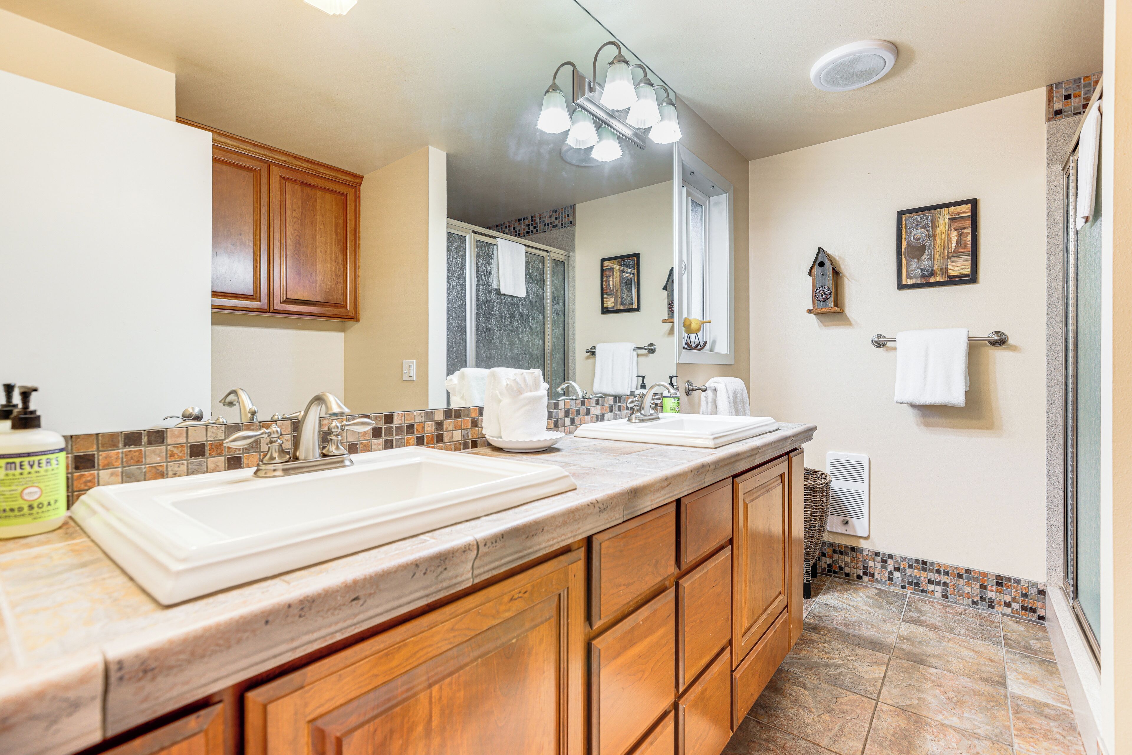 A bathroom with two sinks, wooden cabinets, a large mirror, and a shower area.