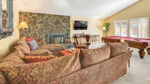 A living room with a stone wall, a pool table, a leather armchair, and a sofa with patterned upholstery. - Bend Golf & Country Club Vacation Home (Bend)