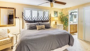 A bedroom with a bed, a ceiling fan, a window with blinds, a bedside table with a lamp, and a mirror on the wall. - Bend Golf & Country Club Vacation Home (Bend)
