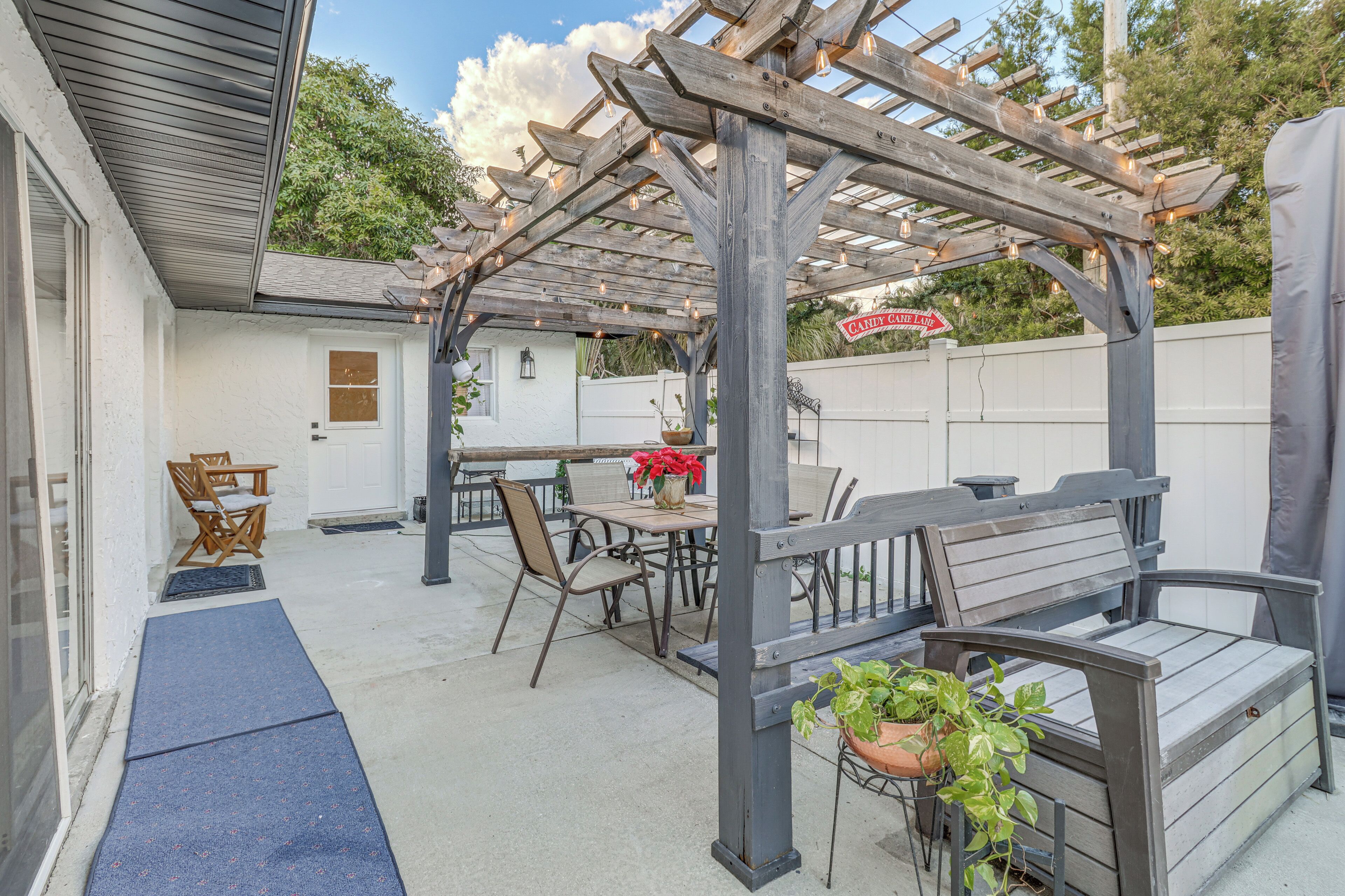 A covered patio area with a wooden pergola, outdoor seating, and a potted plant.