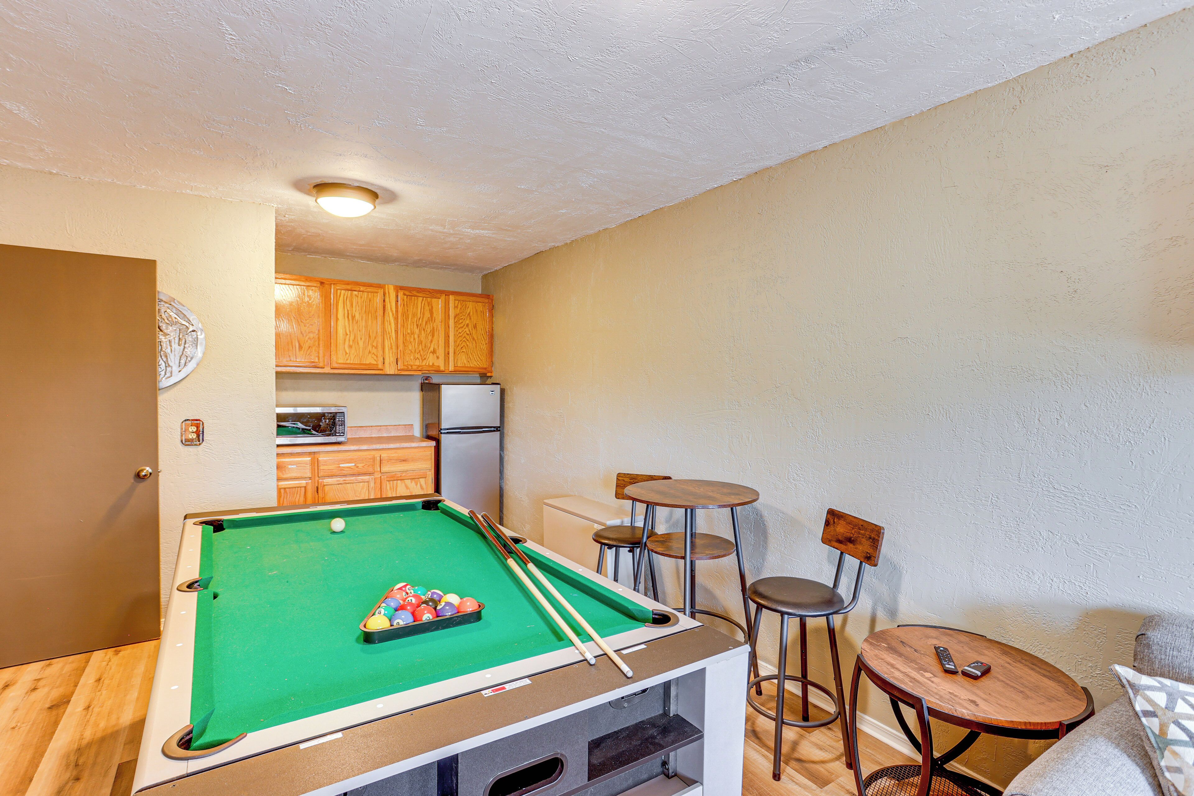 Une table de billard recouverte d’un drap vert, dotée de caissons en bois et accompagnée d’une petite table ronde et de deux chaises.