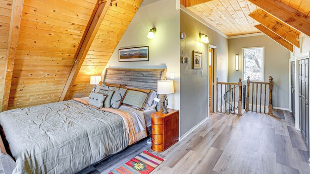 Een slaapkamer met schuine wand, een bed met houten hoofdbord, een nachtkastje en een wandlamp.