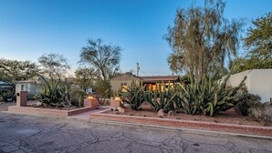 Une maison aux murs extérieurs en briques, entourée de cactus et de plantes du désert, sous un ciel dégagé.