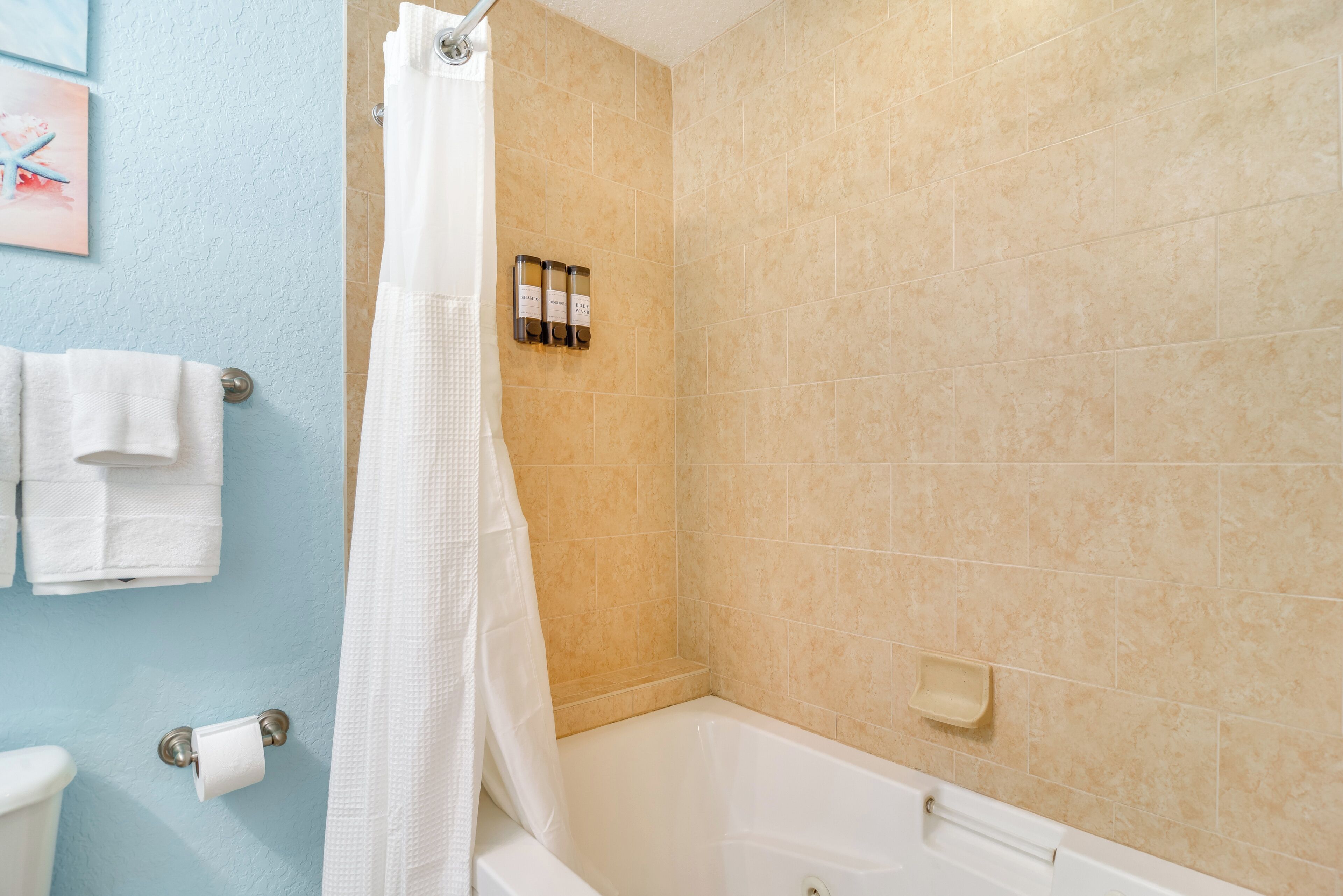 Ein Badezimmer mit Badewanne, beigen Fliesen, einem weißen Handtuchhalter und einer Duschvorhang.