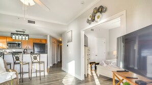 A spacious living area with a large flat-screen TV, wooden flooring, and a kitchen with modern appliances. - Short Walk to Bay & Ocean: Treasure Island Condo (Treasure Island)