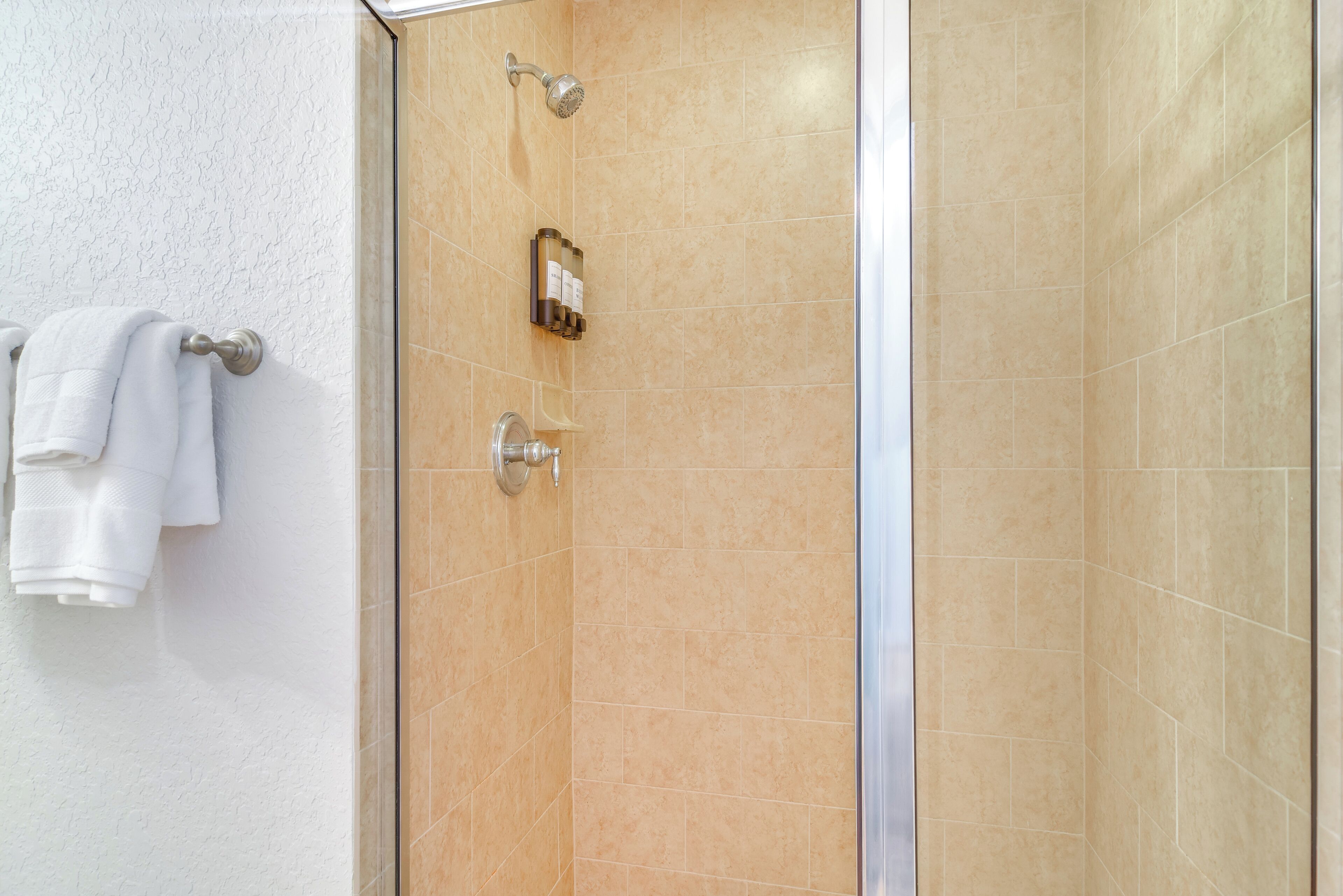 Een douche met beige tegels, een glazen deur en een handdoekrek met witte handdoeken.