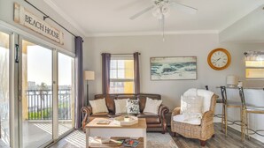 A living room with a sofa, a coffee table, a wicker chair, a painting, and a sign that reads "BEACH HOUSE". - Short Walk to Bay & Ocean: Treasure Island Condo (Treasure Island)